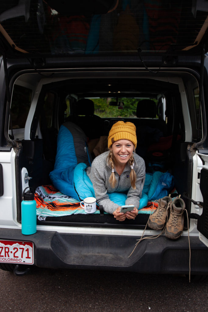 Girl in the back of a Jeep about to go to bed because she found a free camping spot in the US