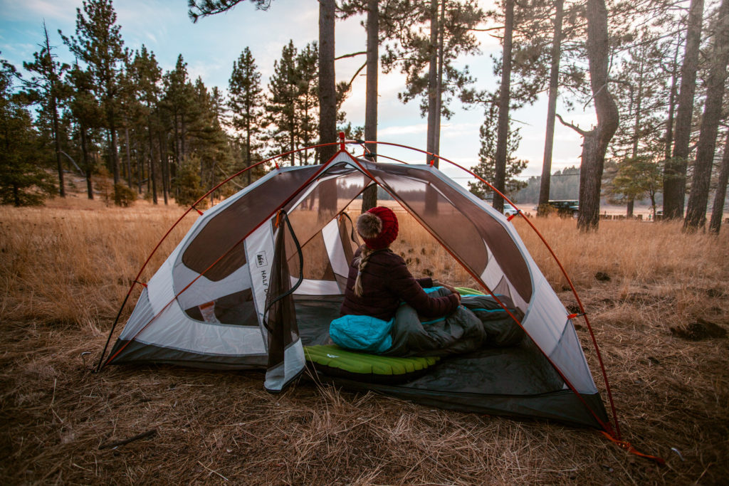 Girl sitting in tent in the woods which is an essential piece of camping equipment