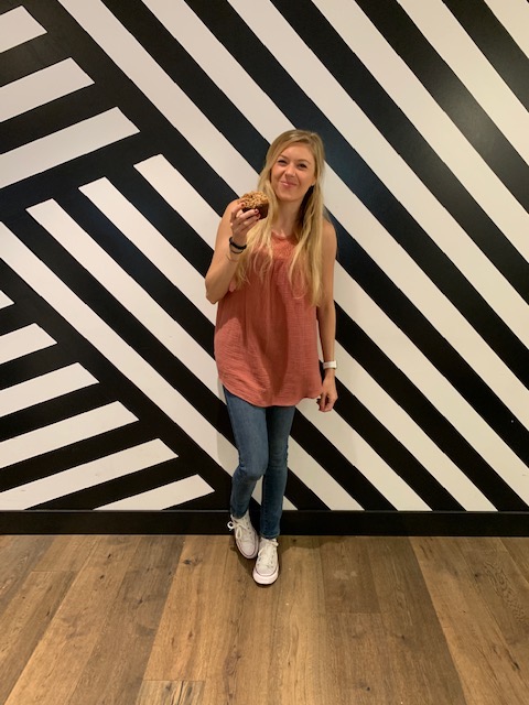 Chelsey holding a muffing in front of a striped wall at Parakeet cafe: one of the cutest coffee shops in San Diego
