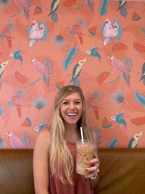 Chelsey holding coffee in front of a Parakeet wall at Parakeet cafe: one of the cutest coffee shops in San Diego