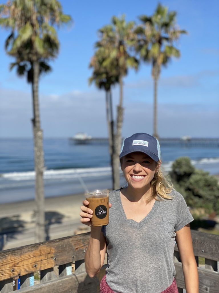 Girl holding iced coffee on the beach with palm trees in the background