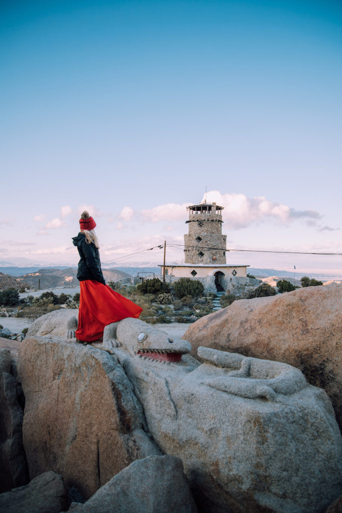 Girl in skirt standing on boulder park rocks with view of the desert view tower in the background