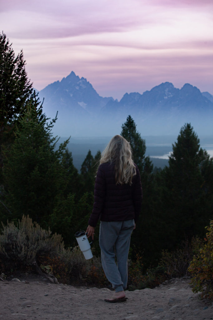 Girl standing in front of the grand Tetons with her water bottle which is an essential item for camping