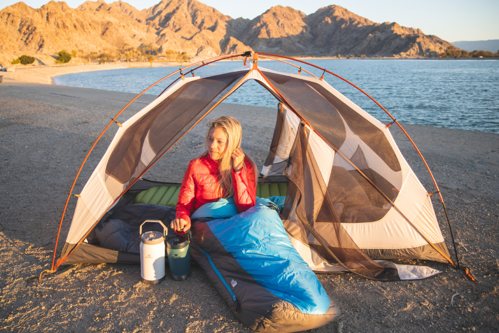 Girl at campsite sitting in her tent with her Stanley Iceflow water jugs