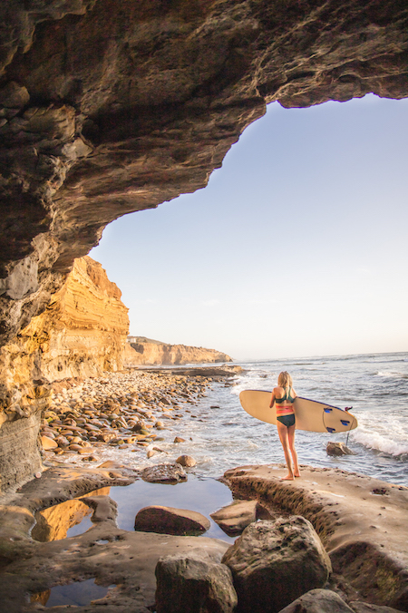 Girl holding a surfboard in a cave on sunset cliffs which is a popular San Diego water sport