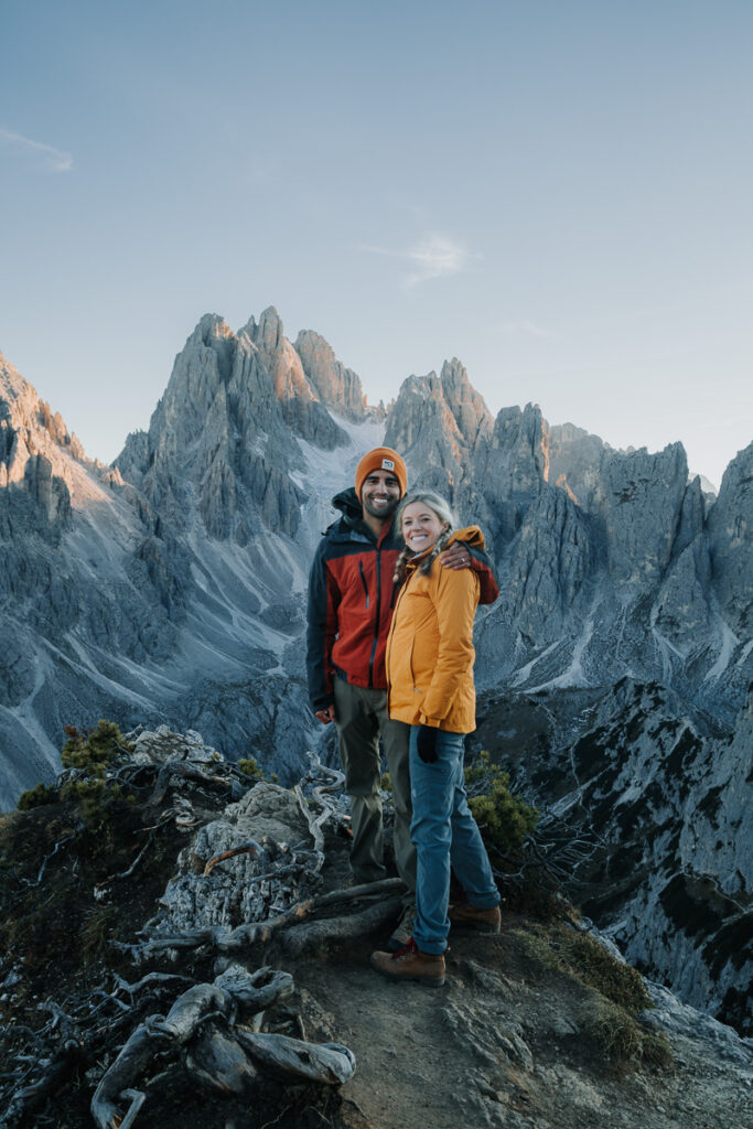 Couple standing atop the Cadini di Misurina hike with the mountain range behind them