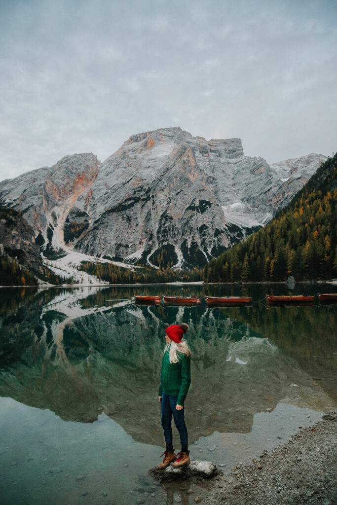 Chelsey Explores standing on a rock looking out at the lake Lago di Braies at sunrise 