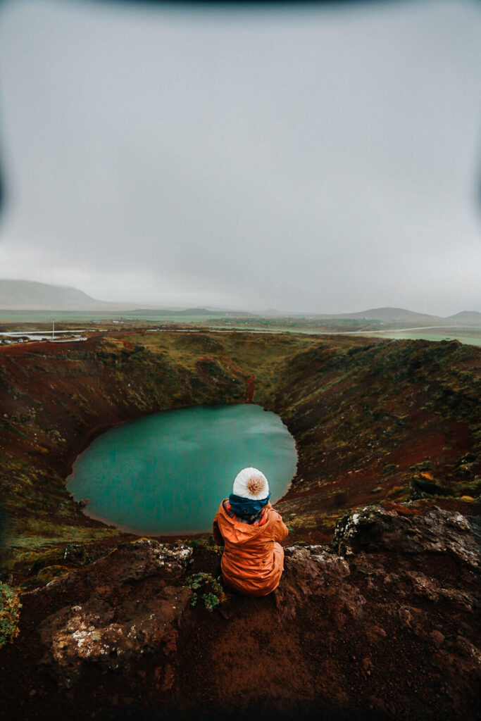 Girl sitting on top of Kerid Crater which is a must stop place to add to your Iceland Itinerary