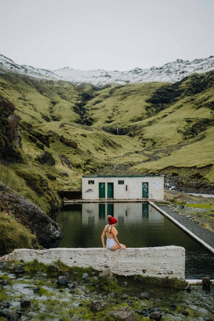 Girl sitting at Seljavallalaug Hot Spring which is a hot spring you have to add to your Iceland itinerary