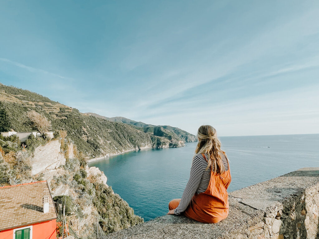 Chelsey Explores sitting on a ledge looking out at the views from the town of Corniglia