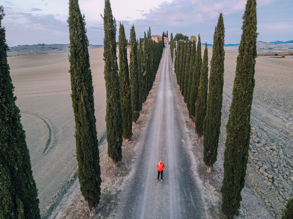 Chelsey Explores standing in the row of trees at the Farmhouse Poggio Covili a stop to make along your Tuscany road trip