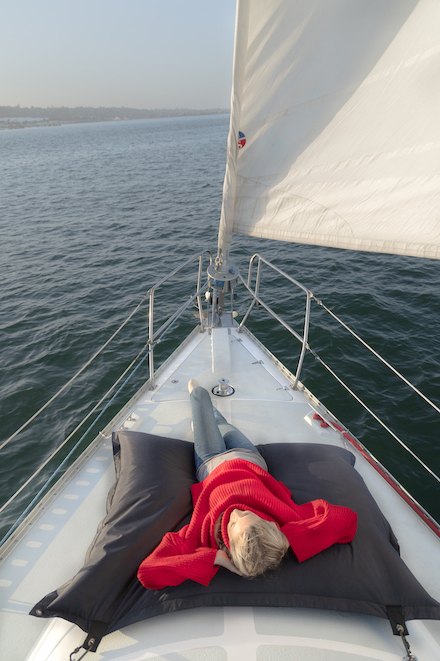 Girl lying down at the front of a sailboat in the San Diego water