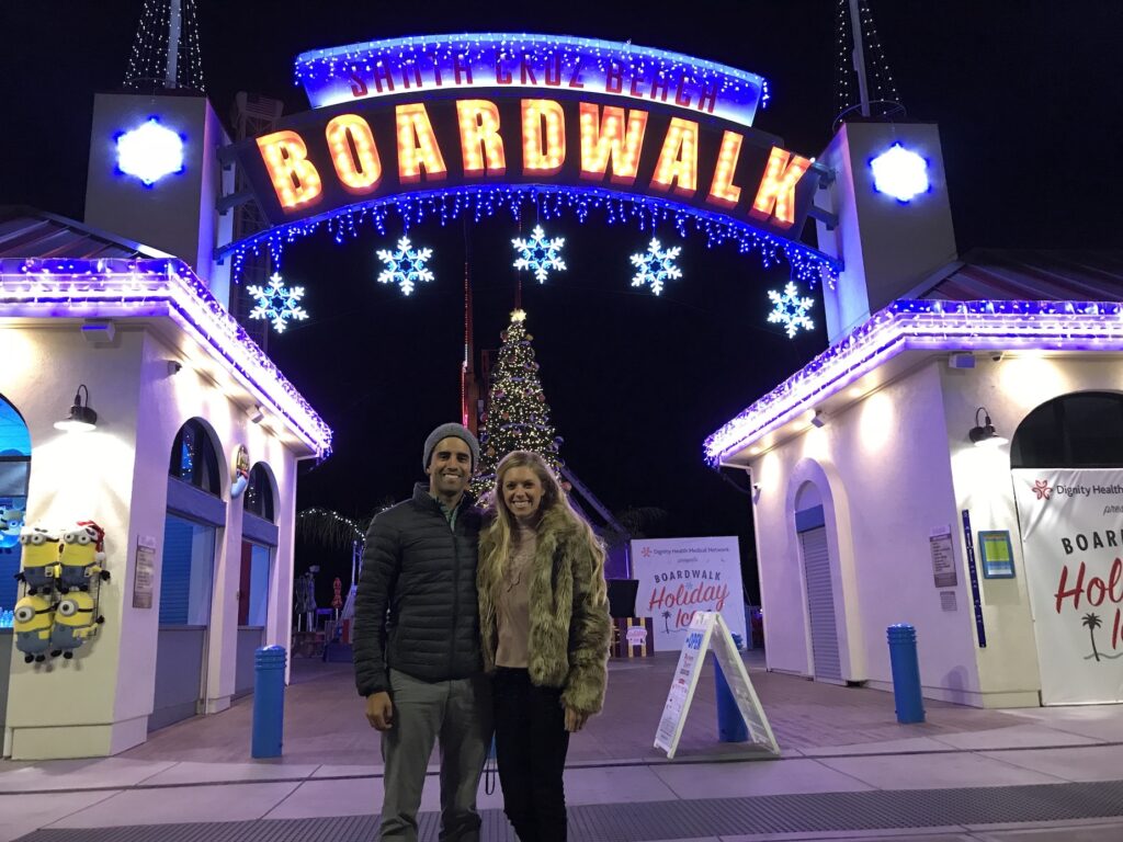 Couple standing in front of the Santa Cruz Boardwalk sign at night