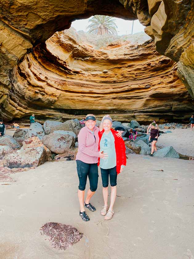 Mom and daughter standing in front of sunset cliffs sea cave